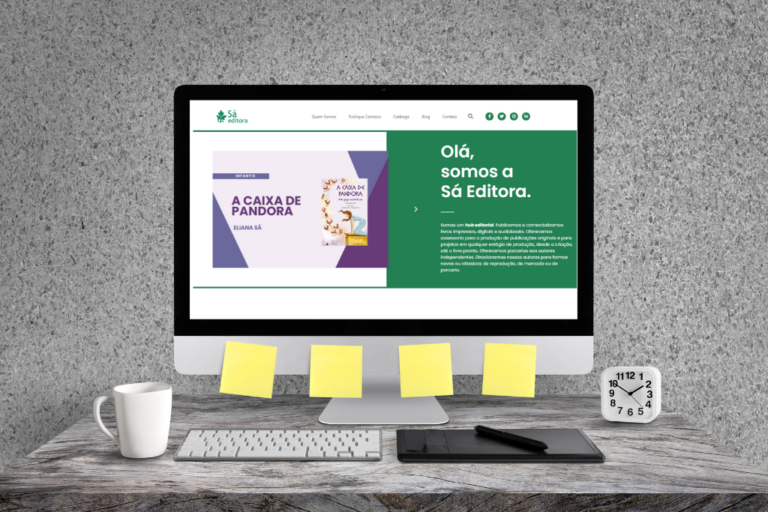 Foto de um computador em cima de uma mesa com xícara e adesivos amarelos colados ao redor da tela. A tela mostra a home do site da Sá Editora.